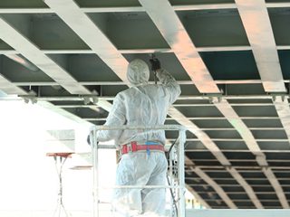 Professional worker in a protective suit and mask paints a bridg Polyurea Coatings Application